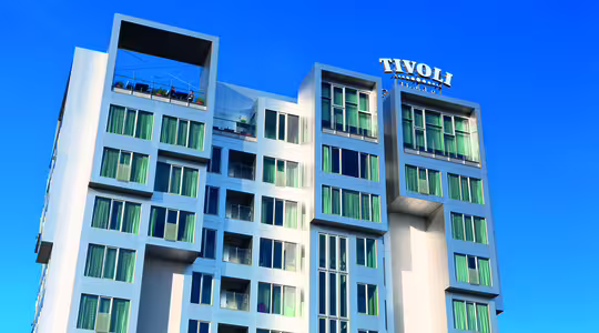 En moderne etagebyggeri med lys facade mod en klar blå himmel. Den øverste etage har en terrasse. Ordet "TIVOLI" er fremtrædende vist på strukturen.