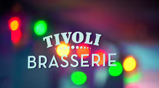 Billedet viser en glaslåge med teksten "Tivoli Brasserie" med hvide bogstaver. Farverige lys i rødt, gult og grønt skaber en sløret effekt i baggrunden.